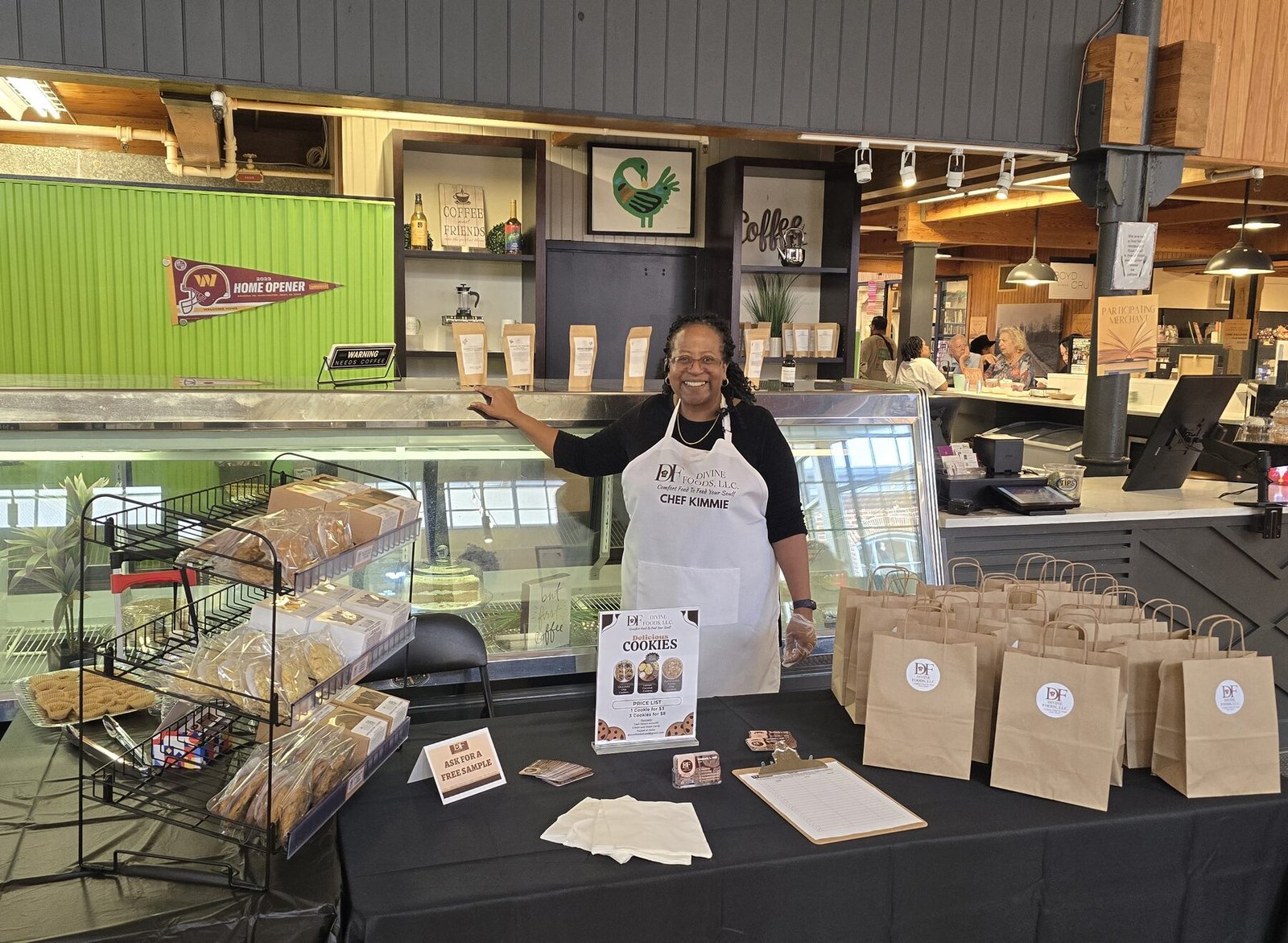 Chef Kimmie behind her table at a Maryland farmers market, kraft bags of cookies stacked and ready